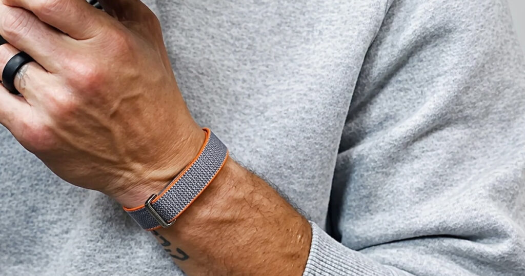 A minimalist, screenless fitness band known as the Fitbit Air, showing a textured nylon strap and low-profile sensor.