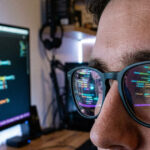 A close up of computer code on a monitor reflecting in a person's glasses.